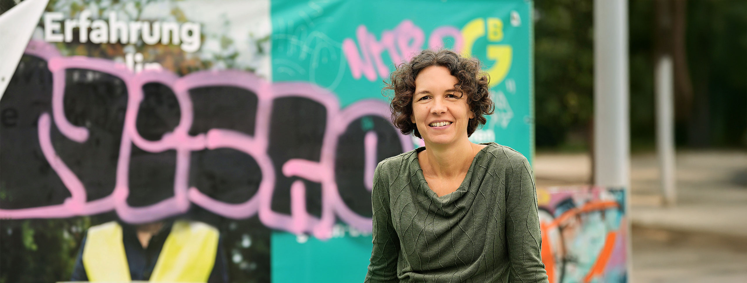 Portrait of Heike Rödel in front of Berlin wall with graffiti.